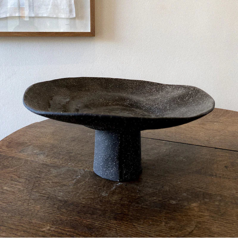 Dark stone pedestal table on a wooden surface with a neutral wall background