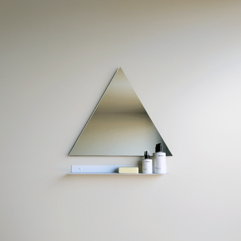 A steel shelf below a triangle bathroom mirror. The modern bathroom shelf holds an artisan soap and two soap dispensers from Mr Price home. The wall mirror and shelf are in a modern bathroom design in Johannesburg