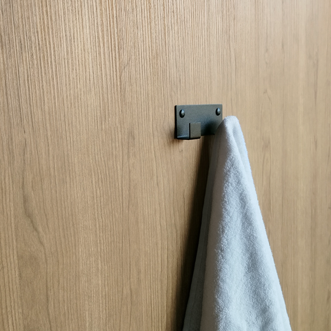 A double black towel hook or wall hook for hanging towels in a bathroom design store in Johannesburg. A white towel is hanging from the black coat hook