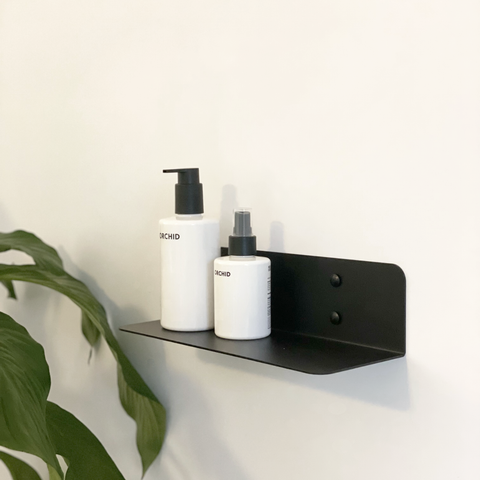 A black steel shelf in a modern bathroom design in Johannesburg. The bathroom shelf has two white soap dispensers from Mr Price Home and an indoor plant