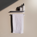 A metal bathroom shelf in a modern bathroom design in Johannesburg. The metal shelf has a cologne bottle and two soap dispenser bottles from Mr Price home. Below the modern bathroom shelf is a steel towel rack that holds a white towel